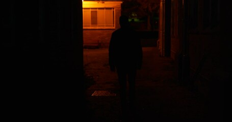 Silhouette male figure walking through dimly lit back streets of city at night