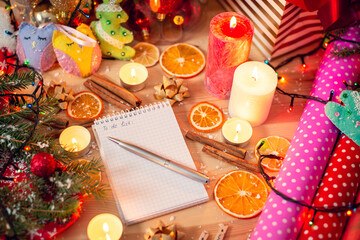 Dried slices of orange, sticks of cinnamon, burning candles, self made christmas decorations, colorful christmas paper and a notebook with inscription To do list in the middle. Festive atmosphere