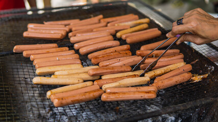 Grilling full of raw fresh sausage on barbecue grill and turned it using tongs on a summer picnic. Preparation of roasted chicken hot dogs on a hot grill stove. Selective focus.