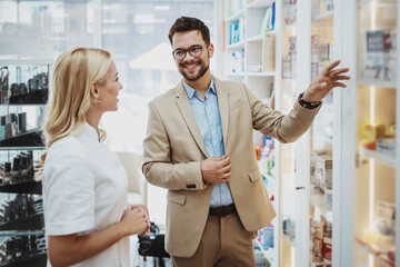 Young business man choosing and buying drugs in a drugstore while talking with attractive female...