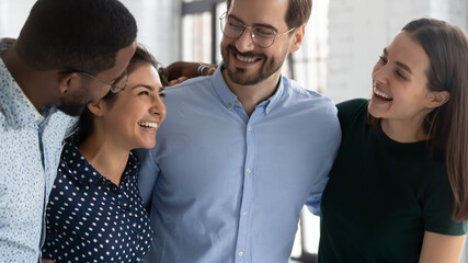 We are together. Happy laughing multiethnic corporate team members young diverse people hugging in office corridor joking having fun demonstrating friendship support unity warm close equal relations