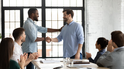 Perfect job. Friendly african american boss or team leader shaking hand of happy excited caucasian employee manager worker on staff meeting at boardroom demonstrating respect greeting with promotion - obrazy, fototapety, plakaty