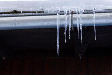 Melting icicles on a cabin rooftop with drainpipe during winter in Austria