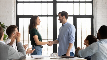 Glad millennial male leader handshaking congratulating happy female employee with professional...