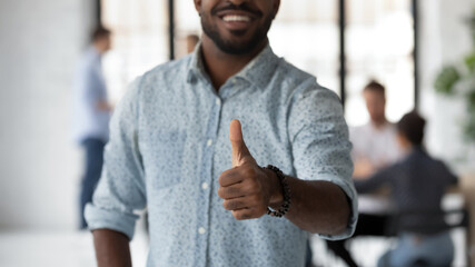 I approve. Close up of smiling satisfied black male employee standing in office demonstrating thumb...