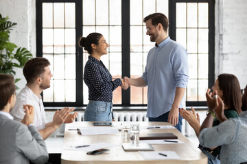 Young caucasian male ceo handshaking with indian female team member on briefing showing respect to her qualification, gratitude for help, recognition of her efforts in developing corporate business - obrazy, fototapety, plakaty