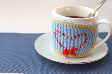 A mug in a knitted blue case, a heart on the case. Valentine's day gift concept.