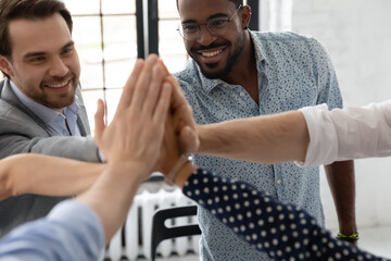 Together we are the power. Close up of happy motivated young multiethnic teammates uniting palms in high five gesture on corporate training or celebrating team achievement after making successful deal