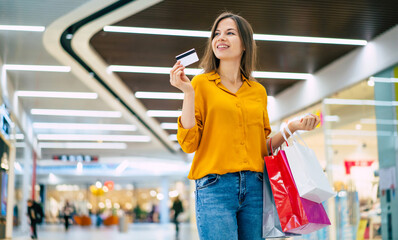 Excited gorgeous smiling young woman is posing with a credit card and shopping bags in the mall