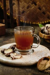 A view of Wedang jahe or warm ginger tea with slices of ginger and scoop of ginger powder as Indonesian traditional herbal drink in brown background. Selective focus with smoke 