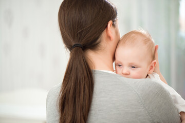 Young mother holding her newborn child. Mom nursing baby. Woman and new born boy relax in a white bedroom.