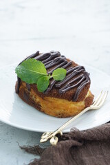 A close up picture of chocolate cheese cake in white plate and shiny background with chocolate glazing and mint leaves for food photography
