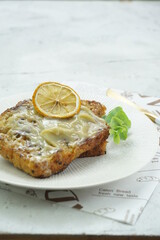 Grainy Roti Bakar Serikaya or French Toast with Kaya Jam topped with sliced lemon and green leaves as garnish in white plate. Copy space, selective focus.