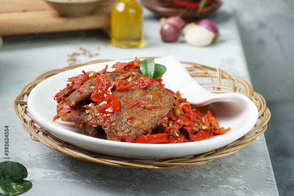 Wall mural Indonesia traditional food, Dendeng Balado or beef jerky mix with chili and herbs and spices placed in white plate with lime leaves on top in the corner of the table