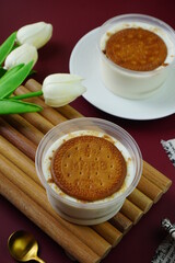 Bannoffee pie in plastic cup as banana fruit and whipping cream as sweet dessert with white flowers as decoration