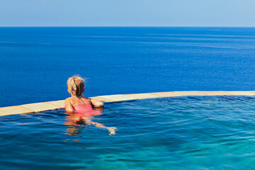 Happy girl have fun on summer beach holiday. Young girl relaxing at edge of infinity swimming pool with sea view from hill top. Healthy family lifestyle, summer travel with kids on tropical islands.