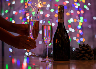 girl holding a bengali fire and a glass of champagne on a beautiful festive bokeh background, consisting of colored out of focus lights on a dark background