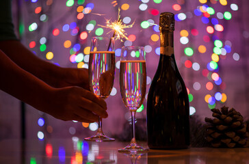 girl holding a bengali fire and a glass of champagne on a beautiful festive bokeh background, consisting of colored out of focus lights on a dark background