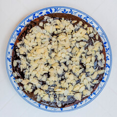 Cocoa and coconut cake covered with chocolate glaze and almond flakes, on a white background