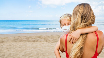 Mother put medical mask on child on sea beach. New rules to wear cloth face covering at public places. Cancelled cruise, tour due coronavirus COVID 19. Family vacation, travel lifestyle at summer 2020