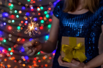 A young woman holds a sparkler and a gift in her hands. Christmas and New Year celebration concept.