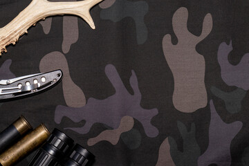 Hunting background. On camouflage background flat lay with hunting accessories. Top view with place for text.
