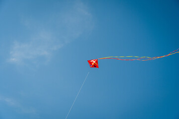A red, flying kite with a long tail under a clear blue sky.