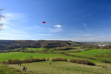 Panoramic view from the Schumisberg, a hill near the city of Leonberg, Germany. A family is flying a red kite that is high in the sky.