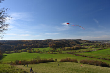 Panoramic view from the Schumisberg, a hill near the city of Leonberg, Germany. A family is flying a red kite that is high in the sky.