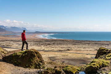 Traveller man standing at Rauðfeldsgjá Gorge Rauofeldsgja ravine (Snaefellsbaer) looking at the ocean beach in a scenic sunny spring day