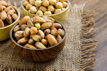 Mixed,crispy, dry nuts in bamboo bowls on wooden table,with jute napkin