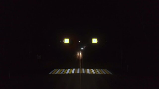 Aerial drone view of night empty crosswalk. Sometimes cars pass. Traffic lights are flashing and road signs are on
