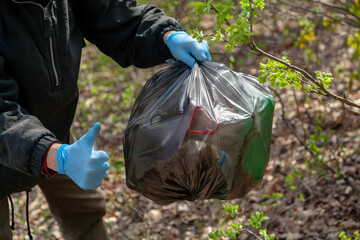 Man in gloves holds bag of trash in forest