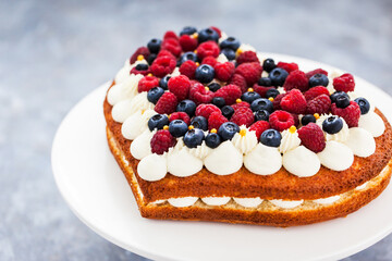 Delicious homemade heart shaped vanilla cake decorated with cream and fresh berries