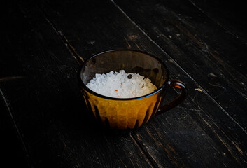 Coarse sea salt in a glass cup, close up. Dark wooden background. 