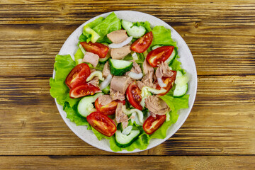 Tasty tuna salad with lettuce and fresh vegetables on wooden table. Top view