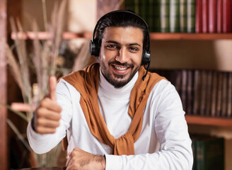 Cheerful Indian Student Guy Gesturing Thumbs Up Sitting Indoor