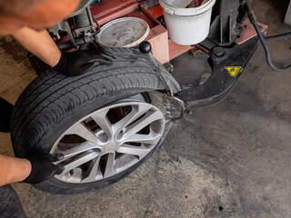 Mechanic with pneumatic wrench unscrews the wheel. Male professional mechanic at a car garage fixing a wheel. Mechanic repairing a car wheel.