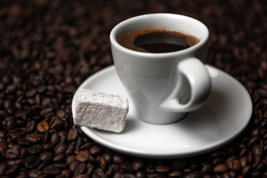 Hot coffee in white cup with Turkish delight on a saucer and coffee beans. © nvcstudio