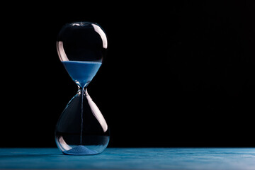 Sandglass, egg timer with blue sand on black background, time passing concept for business deadline