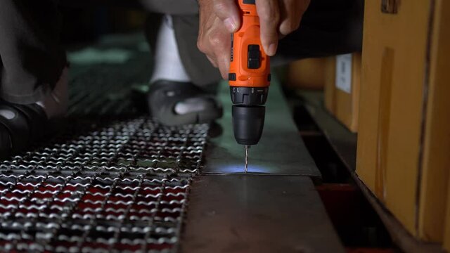 Male worker uses a cordless steel drill to drill a steel grate floor.
