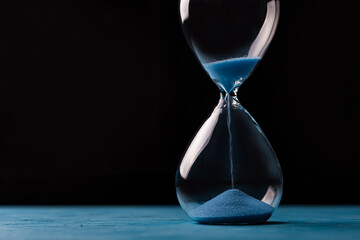 Sandglass, egg timer with blue sand on black background, time passing concept for business deadline