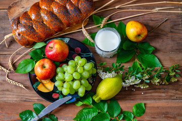 Wicker bun, apples, green grapes, wheat and a glass with milk on a wooden table. Jewish holiday Shavuot.