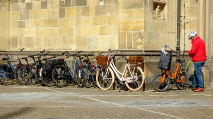 alter Mann parkt Fahrrad an einer Hauswand neben anderen Fahrrädern
