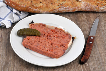 Morceau de pâté de campagne avec un cornichon et un couteau dans une assiette