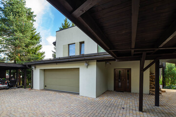 Modern exterior of luxury private house with built-in closed garage. Wooden canopy. Close door. Woodpile near wall.