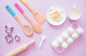Fototapeta na wymiar Ingredients for baking on a lilac background: eggs, flour, whisk, rolling pin. Christmas kitchen atmosphere. View from above. workplace in the kitchen. make cookies for christmas, new year.