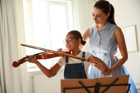Young woman teaching little girl to play violin indoors
