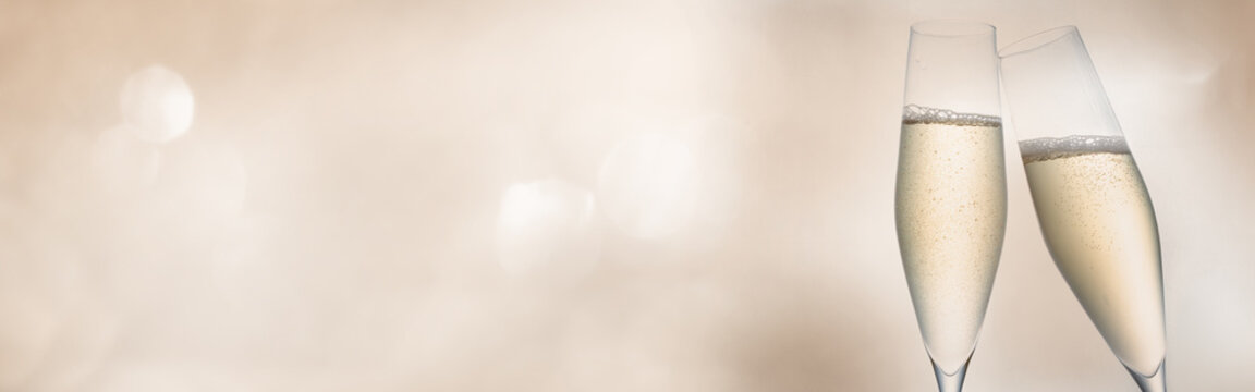 Champagne for festive cheers. Two glasses of sparkling wine in front of tender bright bokeh. Horizontal background for celebrations and invitation cards with space for text.