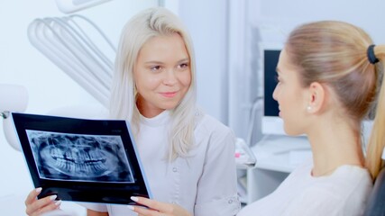 Professional Happy Female Dentist Shows Patient The Situation Of Teeth X-Ray Image Discussion Of The Treatment Plan And Healthy Smile. Concept Of Clean And Healthy Teeth